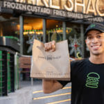 A smiling Shake Shack employee holding a take out bag