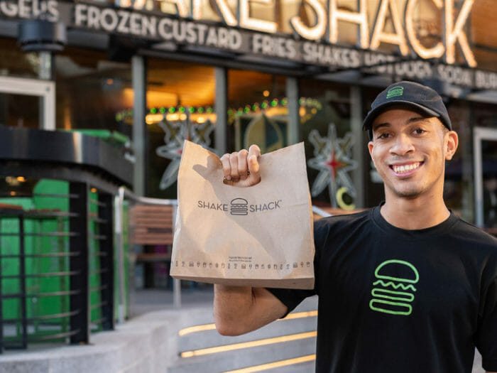 A smiling Shake Shack employee holding a take out bag