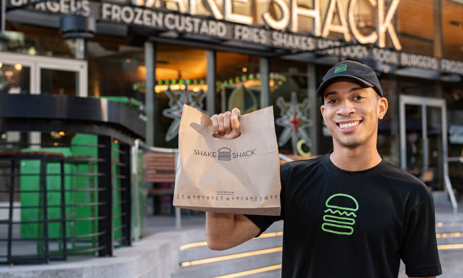 A smiling Shake Shack employee holding a take out bag