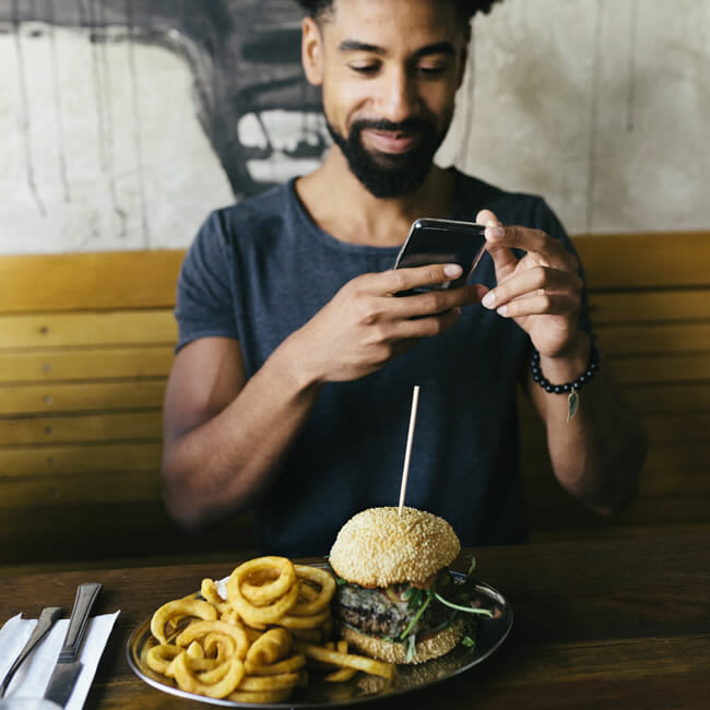 Man in a restaurant taking a picture of his meal with a smartphone