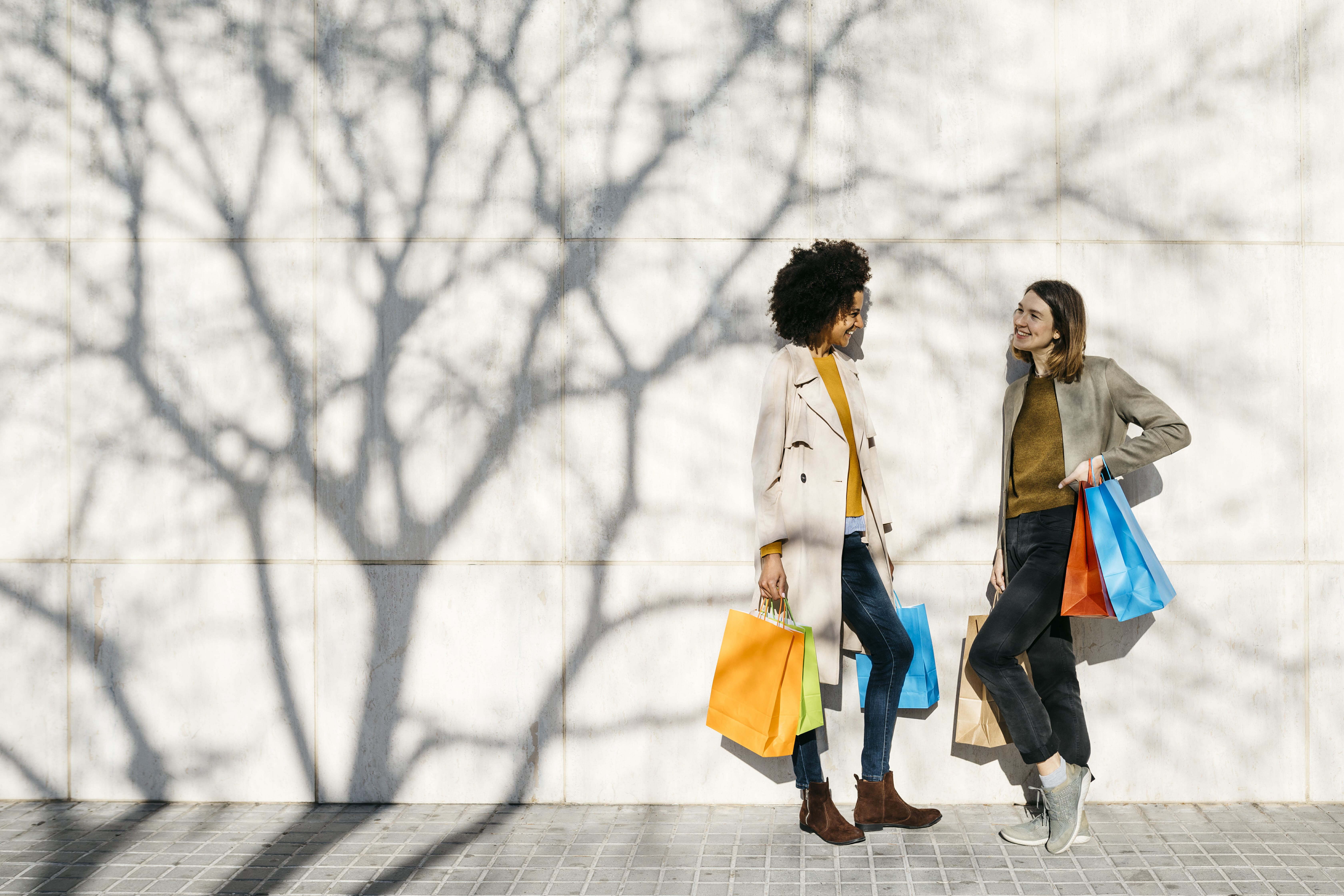 Two happy women with shopping bags standing at a wall talking