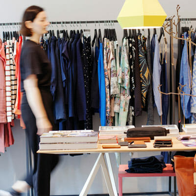 A woman walks by a rack of shirts in a clothing store