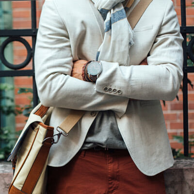 A man's torso wearing a fashionable blazer, a crossbody bag, and a classic watch